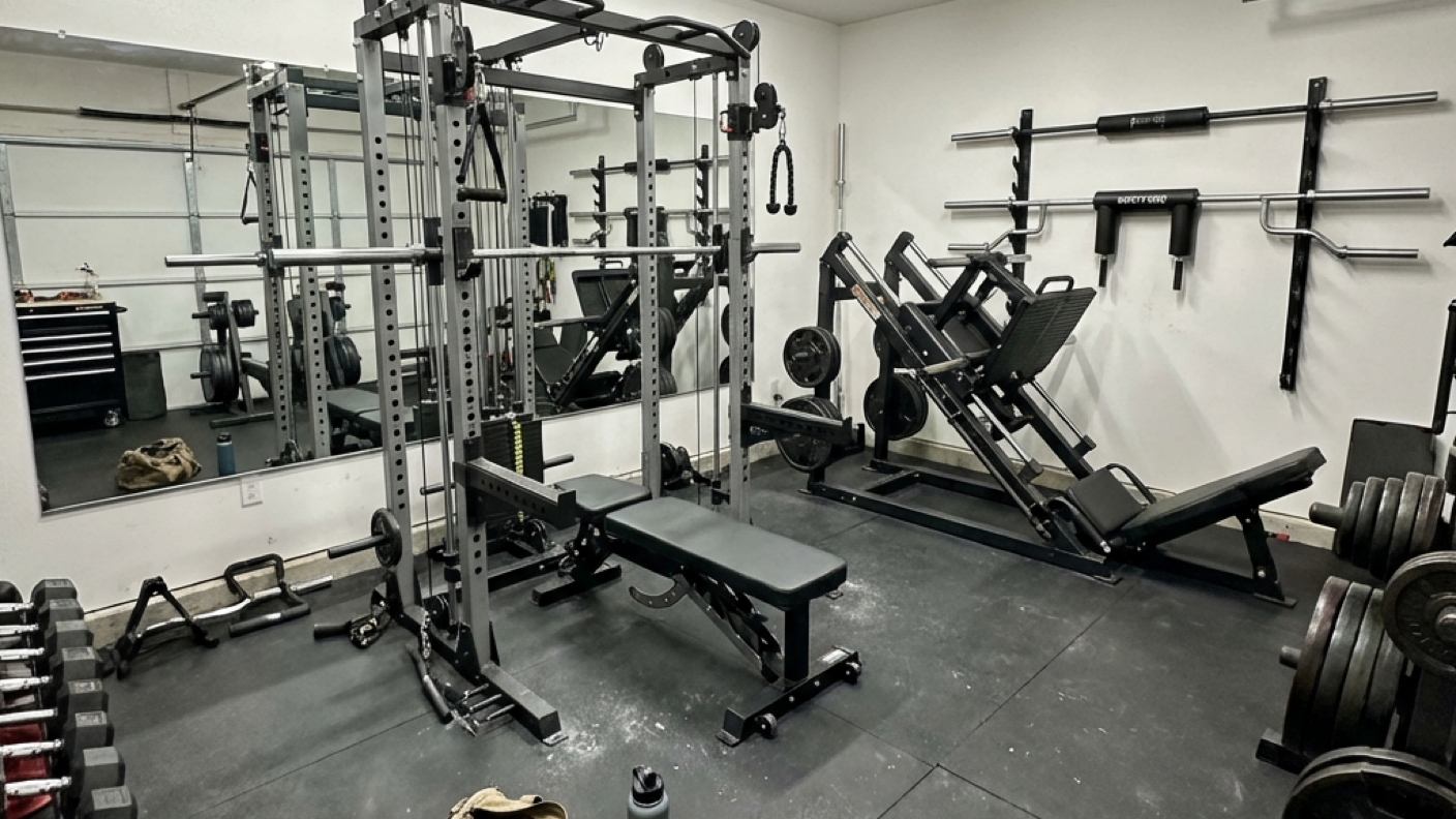 A fully equipped dream home gym with power rack, cable system, leg press, specialty bars, and full rubber flooring